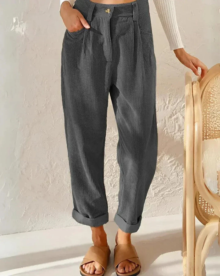Woman wearing loose high-waisted trousers with a tucked-in top, standing in soft light.