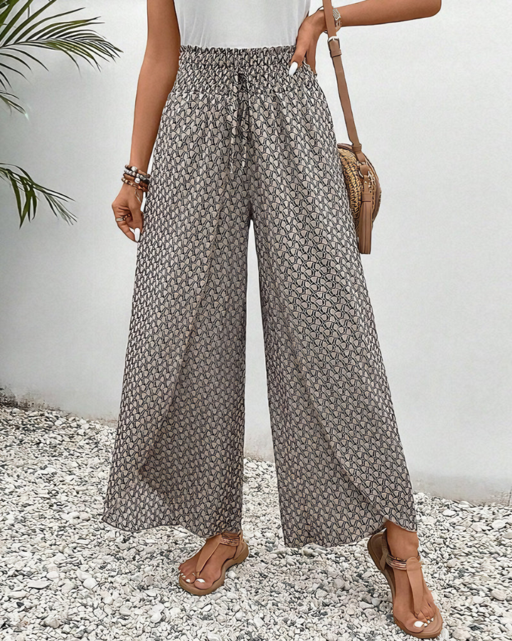 A woman wearing wide, flowing trousers in a beige-and-black geometric print with an elastic drawstring waist.