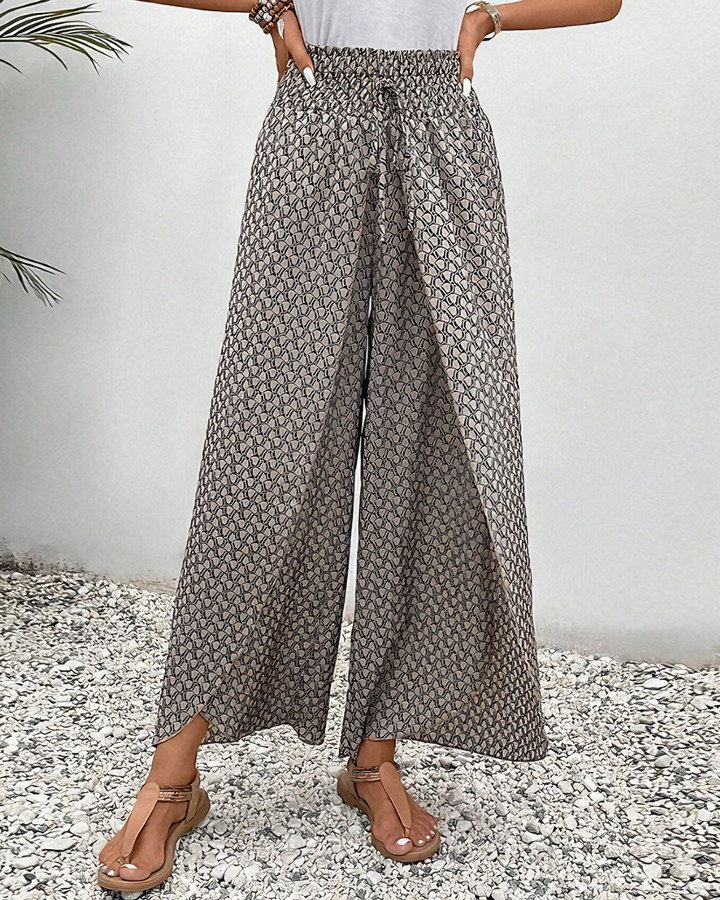 A woman wearing wide, flowing trousers in a beige-and-black geometric print with an elastic drawstring waist.