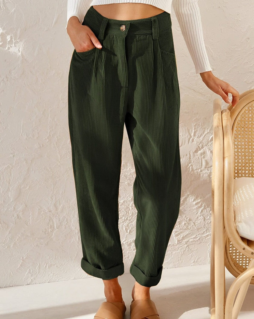 Woman wearing loose high-waisted trousers with a tucked-in top, standing in soft light.