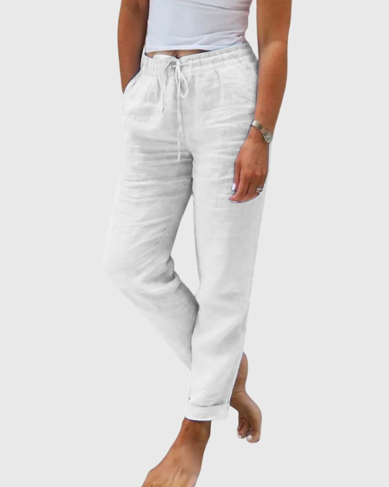 Woman wearing tailored trousers with a smart top, standing confidently in soft light.