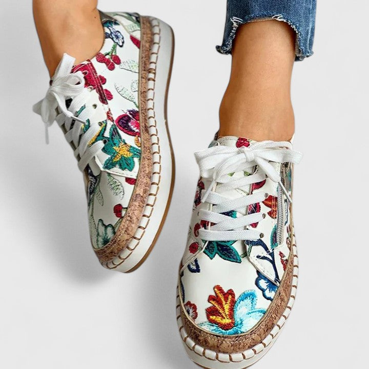 A woman wearing floral lace-up orthopaedic trainers with a side zip and platform sole.