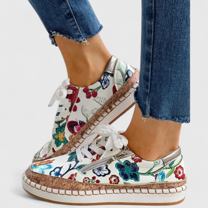 A woman wearing floral lace-up orthopaedic trainers with a side zip and platform sole.