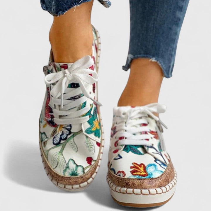 A woman wearing floral lace-up orthopaedic trainers with a side zip and platform sole.