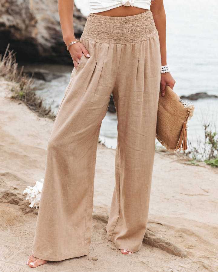 A woman walking by the sea in wide-leg beach trousers with a relaxed, breezy summer look.