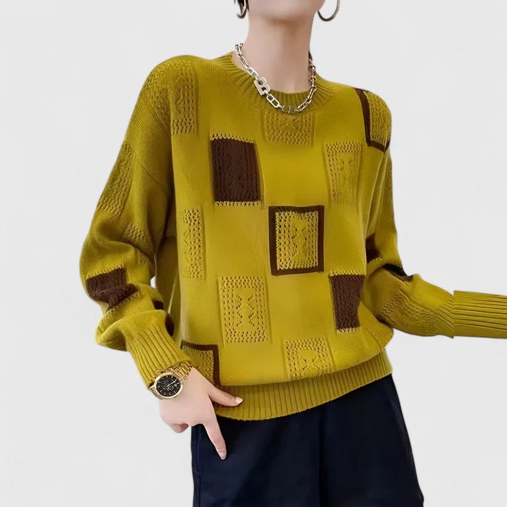 A woman wearing a white jumper with black geometric squares and openwork detailing, round neck.