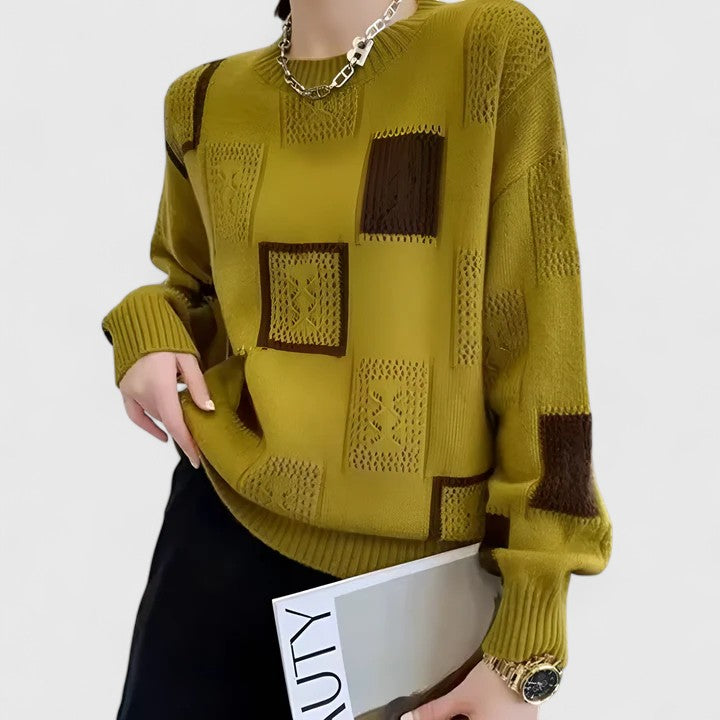 A woman wearing a white jumper with black geometric squares and openwork detailing, round neck.