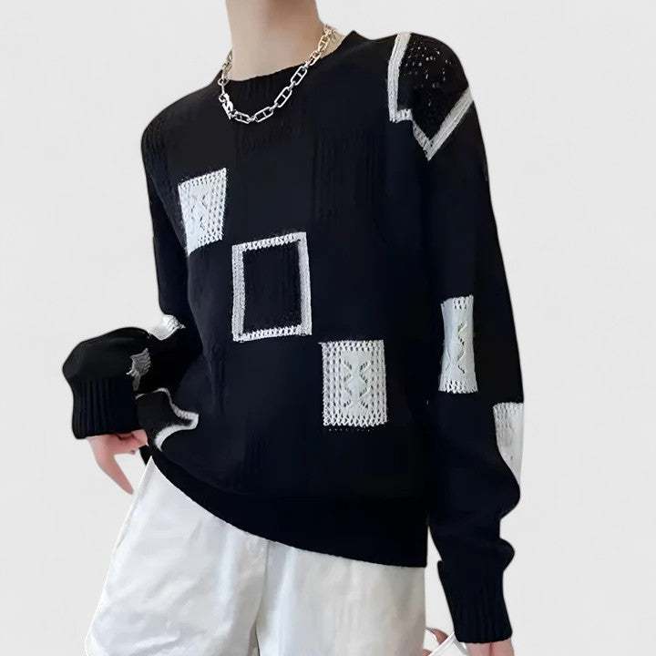 A woman wearing a white jumper with black geometric squares and openwork detailing, round neck.