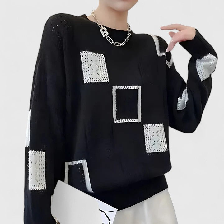 A woman wearing a white jumper with black geometric squares and openwork detailing, round neck.