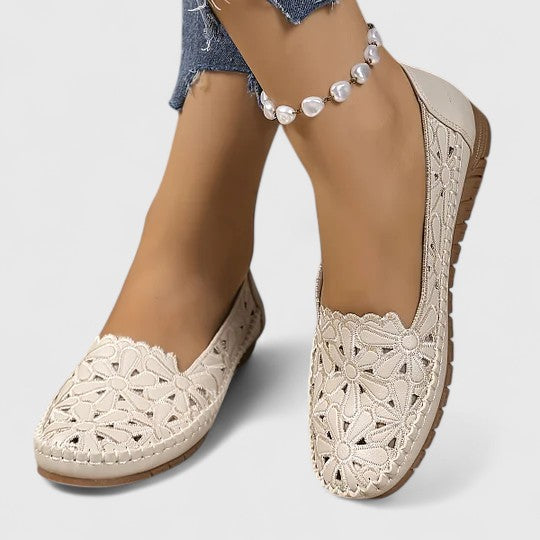 A woman wearing white floral cut-out slip-on flats on a warm, sunny day.