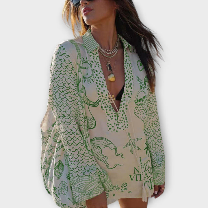 Woman walking on the beach in a relaxed tunic dress with playful maritime print and tie collar.