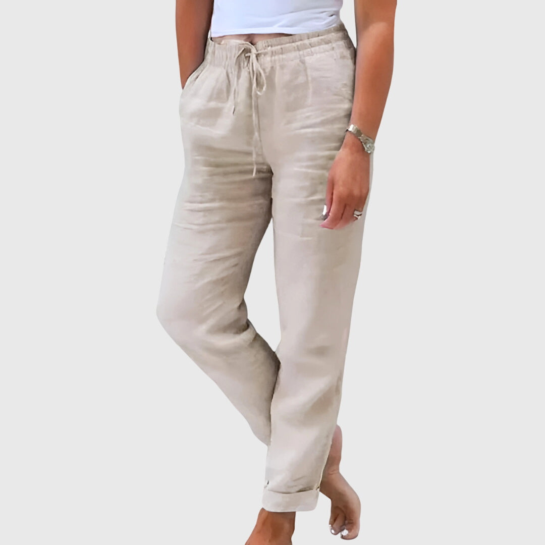 Woman wearing tailored trousers with a smart top, standing confidently in soft light.