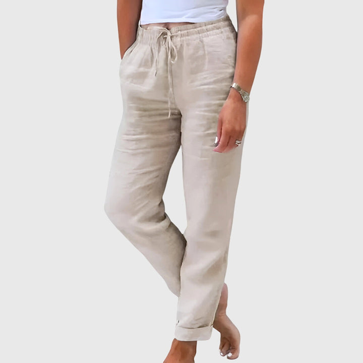 Woman wearing tailored trousers with a smart top, standing confidently in soft light.