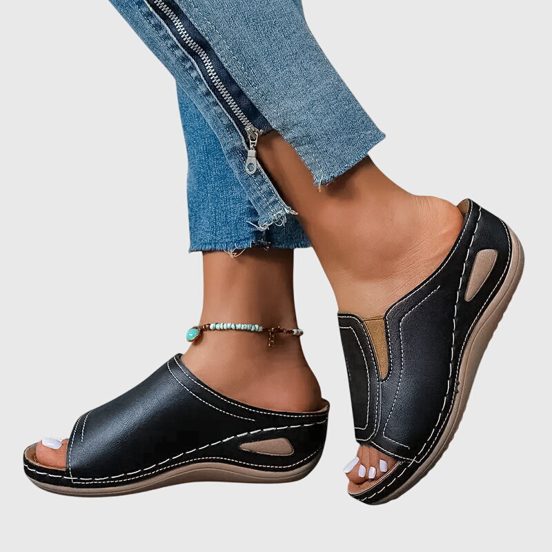 A woman walking confidently in charcoal ergonomic comfort sandals with a broad, cushioned sole.