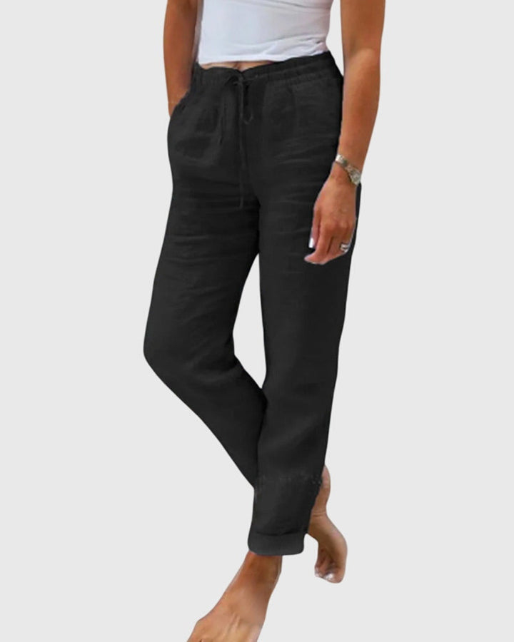 Woman wearing tailored trousers with a smart top, standing confidently in soft light.