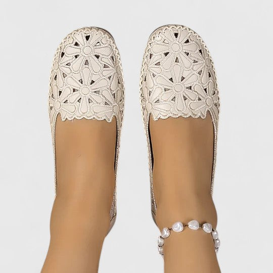 A woman wearing white floral cut-out slip-on flats on a warm, sunny day.