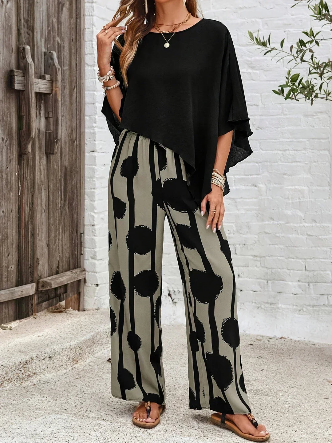 A woman wearing a draped asymmetric top with printed high-waisted wide-leg trousers.