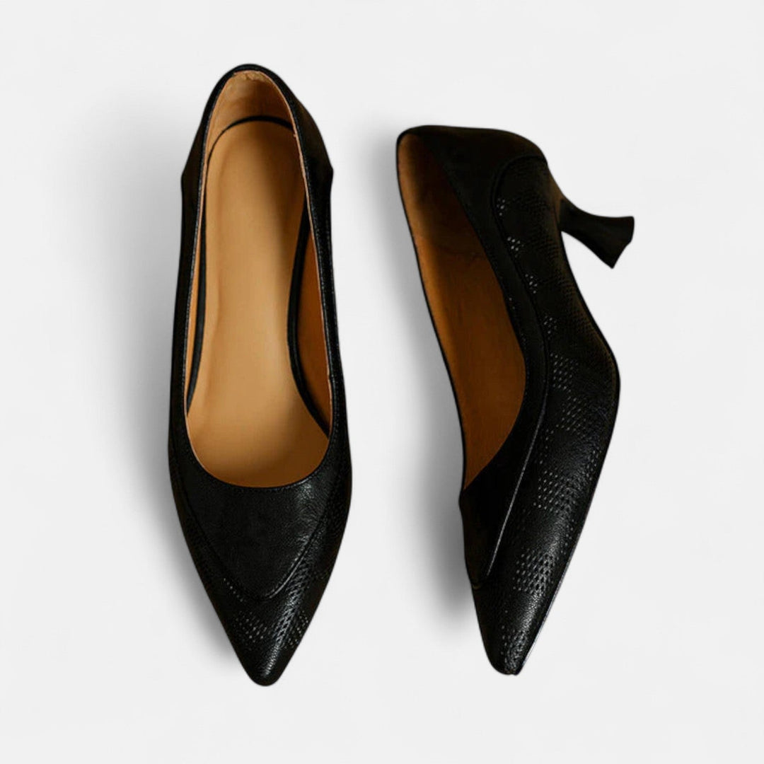 A woman wearing black pointed kitten-heel pumps with a subtle embossed finish.