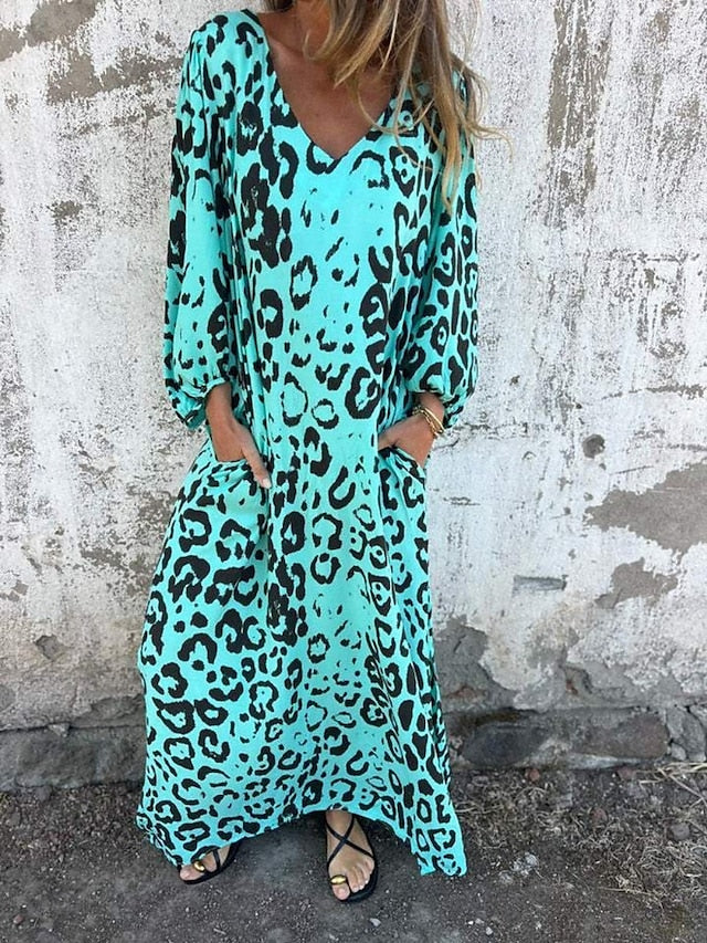 Woman in the Julia leopard print maxi dress with long sleeves and a V-neckline, walking along the shoreline.