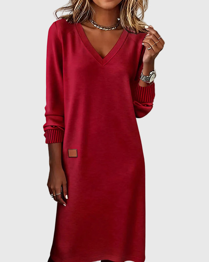 Woman wearing the Emma flowing elegant dress in beige, standing relaxed and smiling.