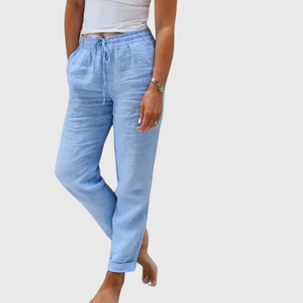 Woman wearing tailored trousers with a smart top, standing confidently in soft light.