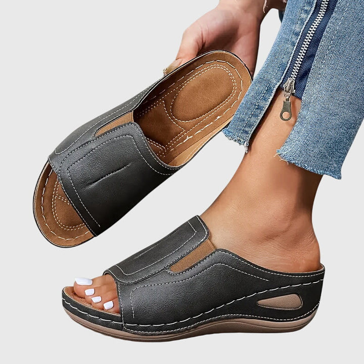 A woman walking confidently in charcoal ergonomic comfort sandals with a broad, cushioned sole.