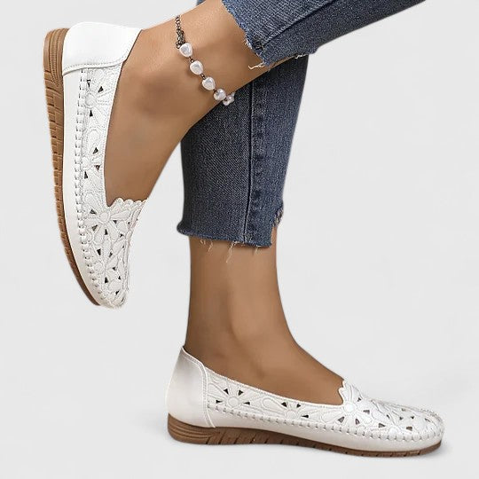 A woman wearing white floral cut-out slip-on flats on a warm, sunny day.