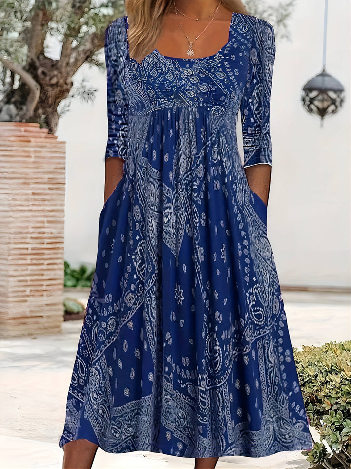 A woman wearing the Maureen long sleeve grey paisley midi dress with a square neckline and flowing skirt, styled for a relaxed day out.