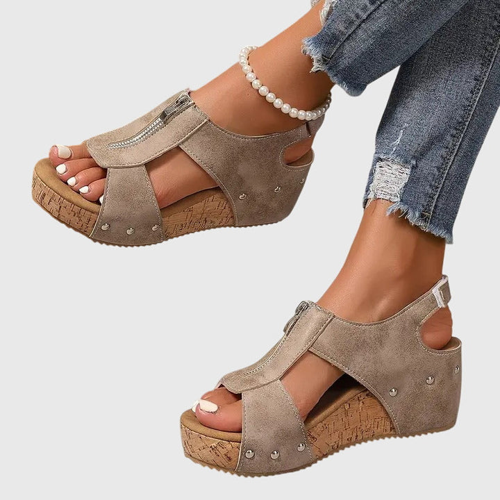 A woman wearing black zip-front wedge sandals with a cushioned footbed and open toe.