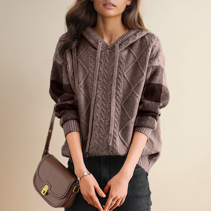 A woman wearing a soft cable-textured hooded jumper, cosy and warm with the hood down.