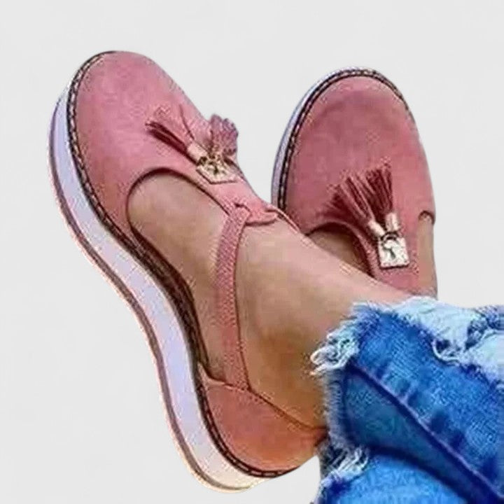A woman wearing elegant supportive loafers with golden detail and tailored trousers, looking polished and at ease.