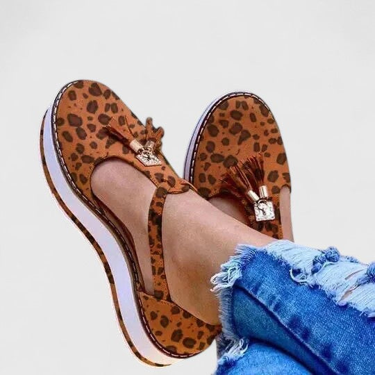 A woman wearing elegant supportive loafers with golden detail and tailored trousers, looking polished and at ease.