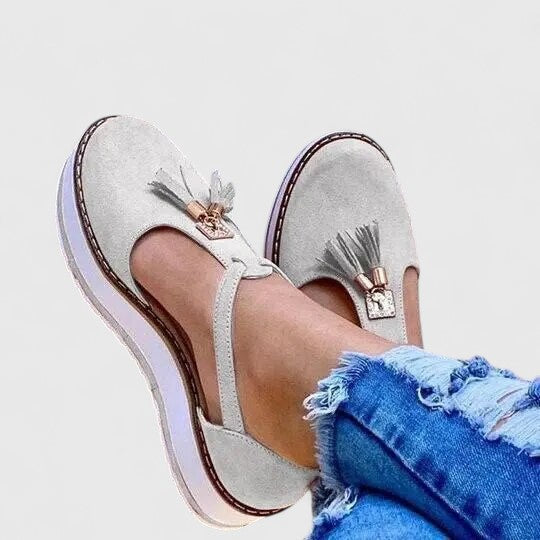A woman wearing elegant supportive loafers with golden detail and tailored trousers, looking polished and at ease.