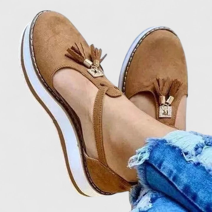 A woman wearing elegant supportive loafers with golden detail and tailored trousers, looking polished and at ease.