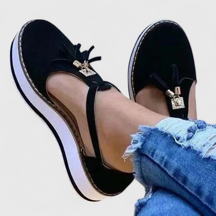 A woman wearing elegant supportive loafers with golden detail and tailored trousers, looking polished and at ease.