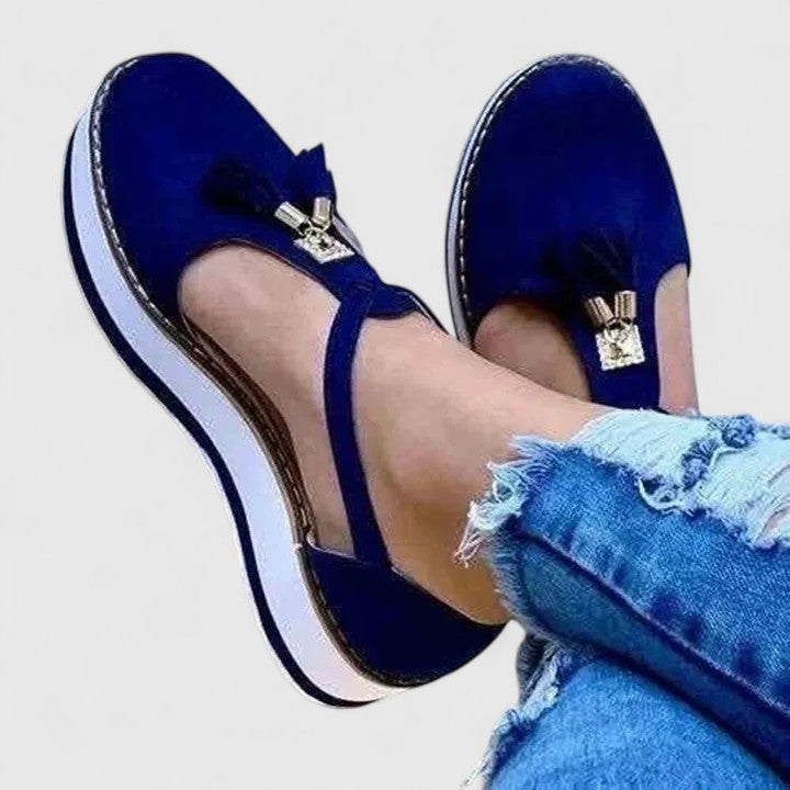 A woman wearing elegant supportive loafers with golden detail and tailored trousers, looking polished and at ease.