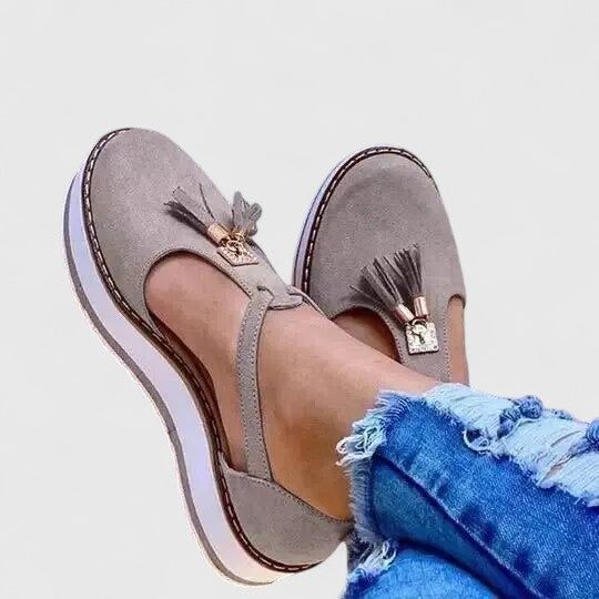 A woman wearing elegant supportive loafers with golden detail and tailored trousers, looking polished and at ease.