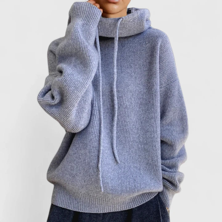 A woman wearing a cosy soft green hoodie with a drawstring hood and white trousers.