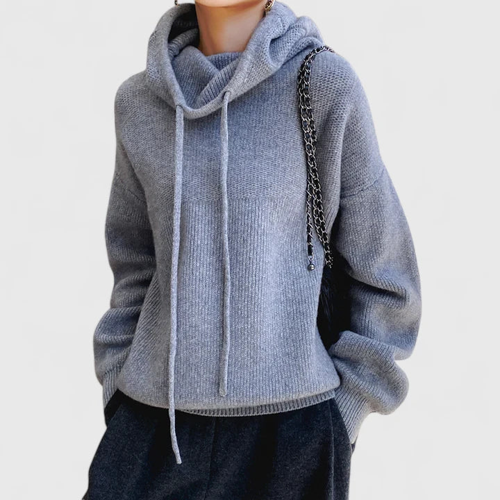 A woman wearing a cosy soft green hoodie with a drawstring hood and white trousers.