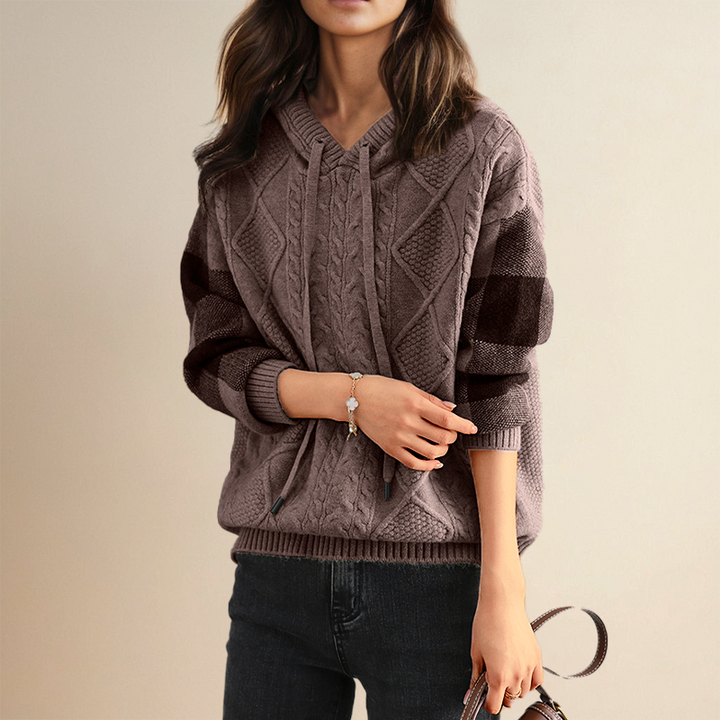 A woman wearing a soft cable-textured hooded jumper, cosy and warm with the hood down.