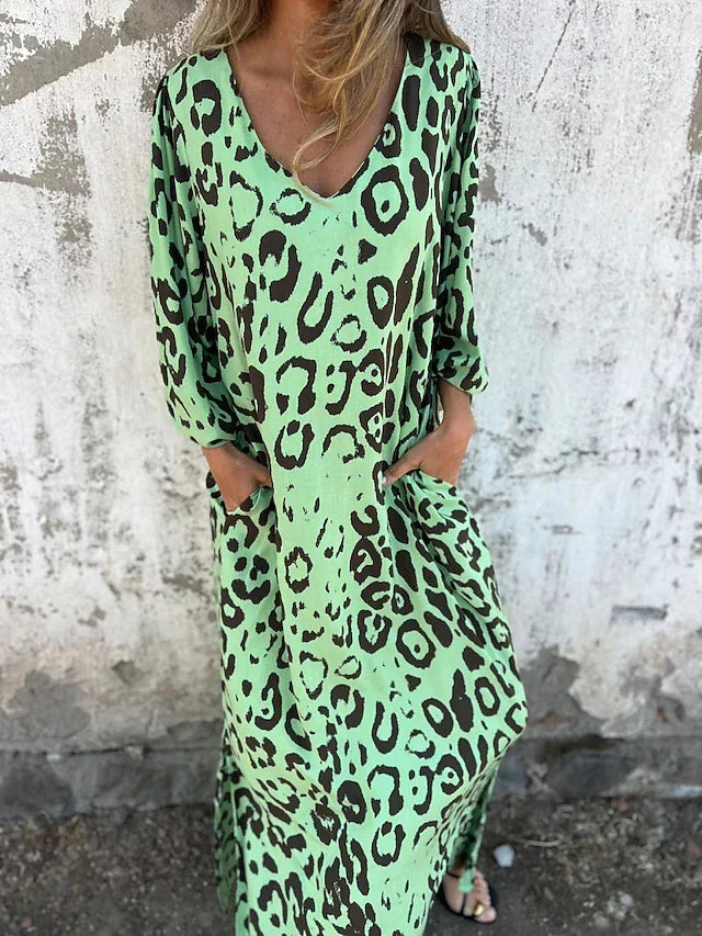 Woman in the Julia leopard print maxi dress with long sleeves and a V-neckline, walking along the shoreline.