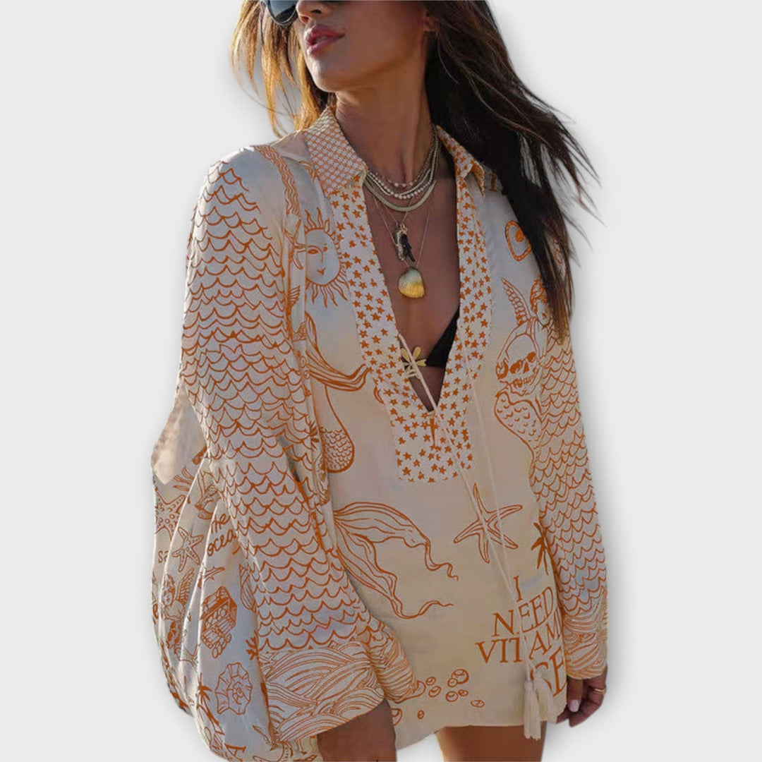 Woman walking on the beach in a relaxed tunic dress with playful maritime print and tie collar.