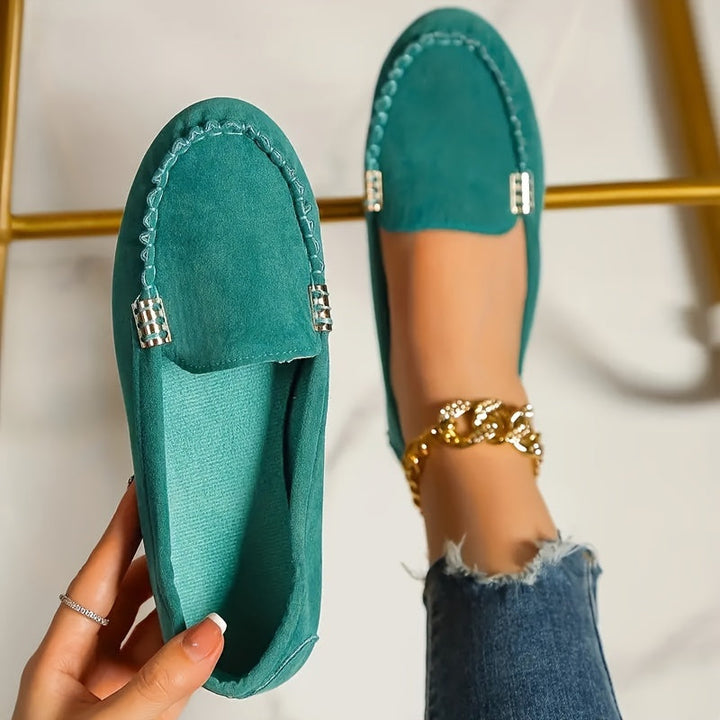 A woman in a ballet-flat loafer stepping lightly along a bright pavement.