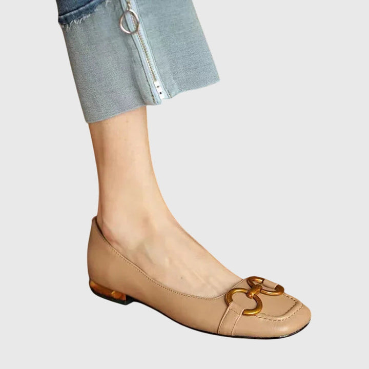 A pair of black slip-on flats with a polished gold ring detail across the toe.