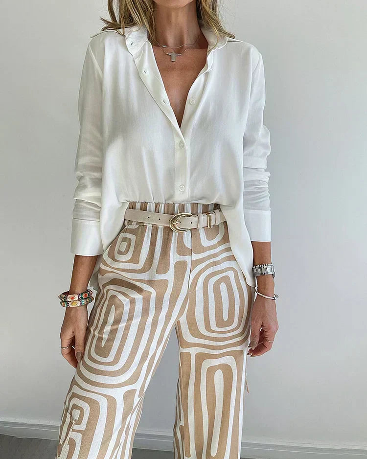 A woman wearing a plain button-up top with geometric-print trousers and a belt at the waist.