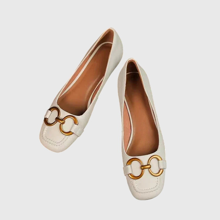 A pair of black slip-on flats with a polished gold ring detail across the toe.