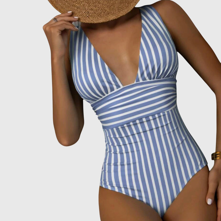 A woman walking by the sea in a bright printed swimsuit, relaxed and glowing in the sun.