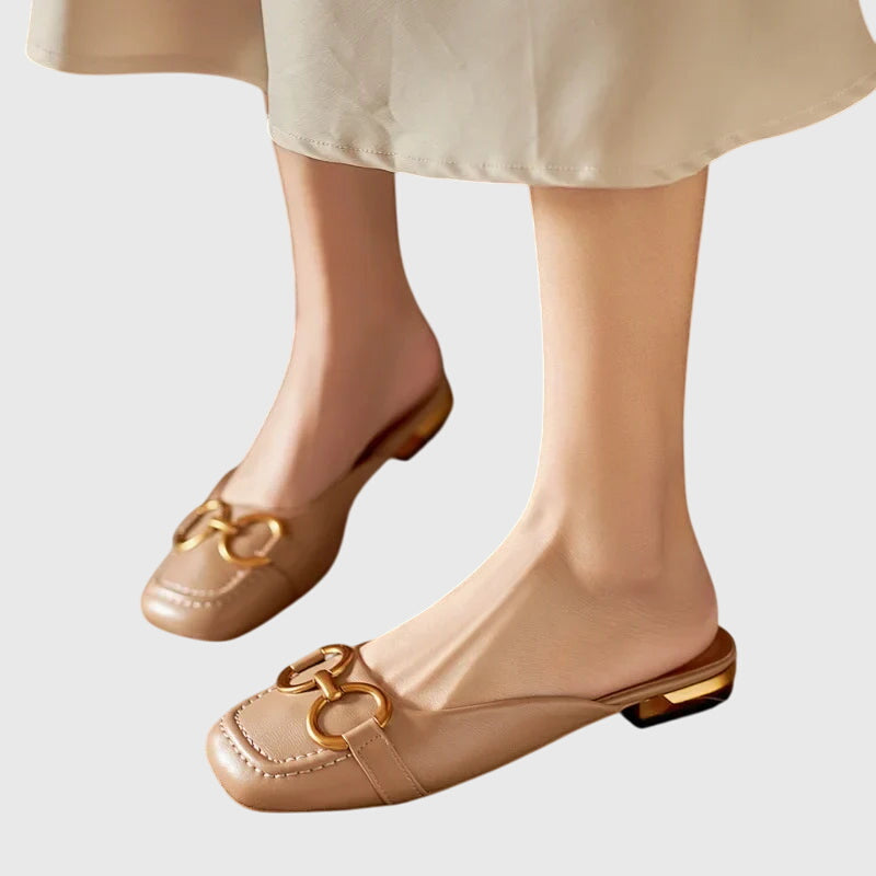 A cream closed-toe mule with a gold horsebit ring detail and a low heel.