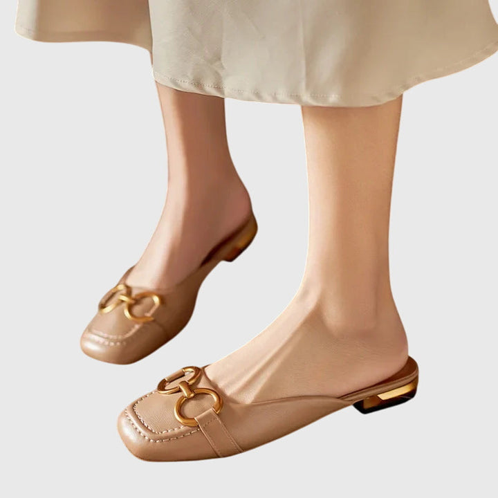 A cream closed-toe mule with a gold horsebit ring detail and a low heel.