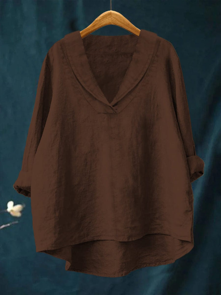A woman wearing an elegant plain summer blouse with a flowing drape, styled with trousers.